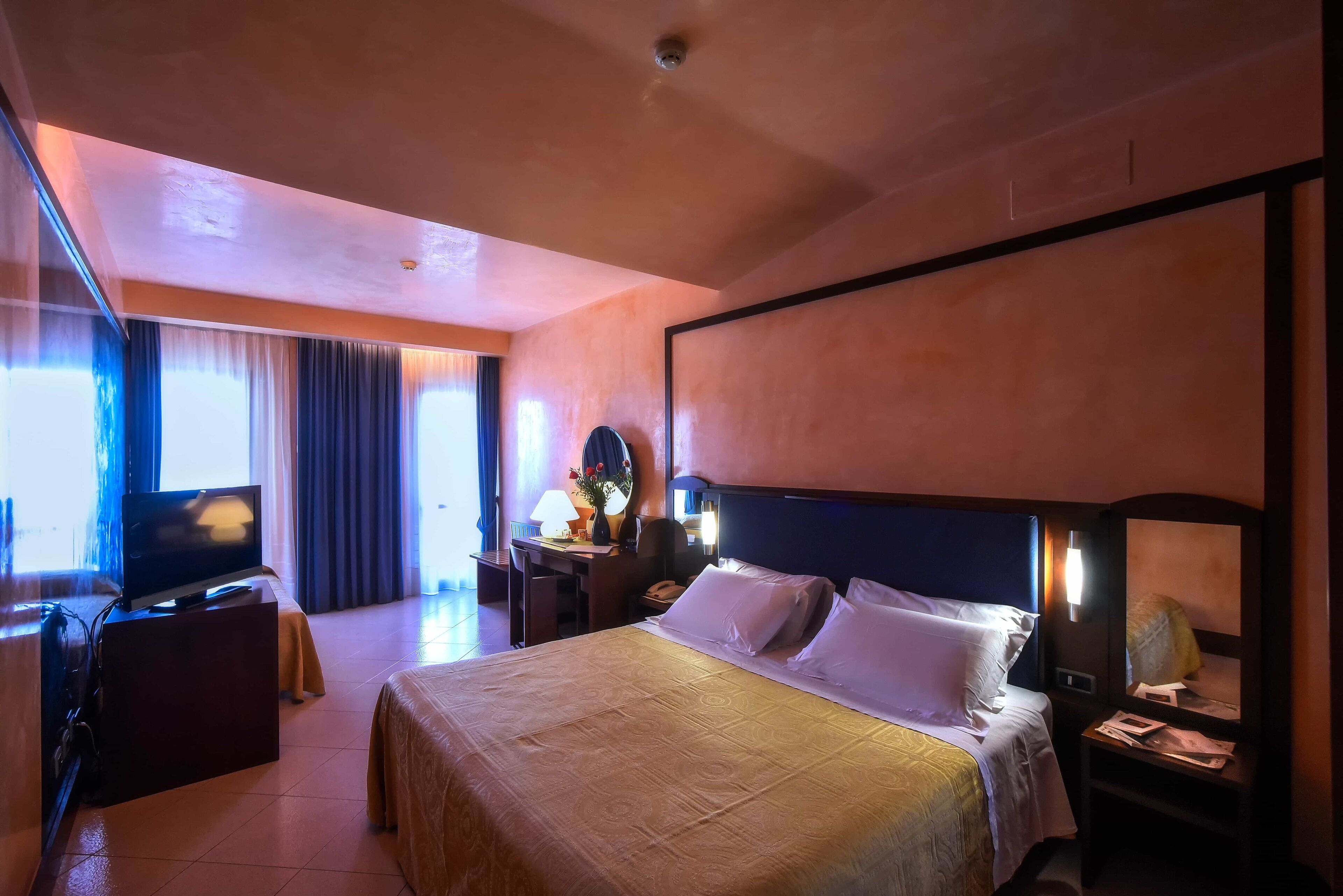 Habitació d'hotel amb un llit gran, un escriptori amb televisió i una tauleta de nit amb una làmpada.