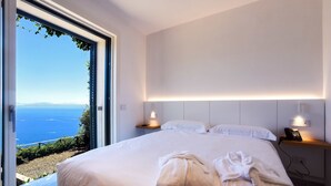 A modern hotel room with a large bed, two bedside tables with lamps, and a view of the sea through a glass door. - Hotel Graal (Ravello)