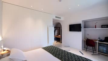 Habitación de hotel con cama, mesita de noche, lámpara, armario, escritorio con silla y televisor en la pared.