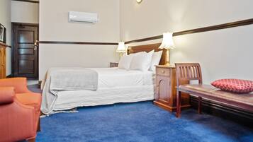 A bedroom with a bed, bedside table, lamp, chair, and a red pillow.