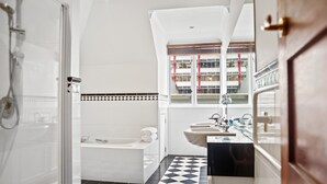 A bathroom with a checkered floor, a bathtub, a sink, and a window with a view of buildings.