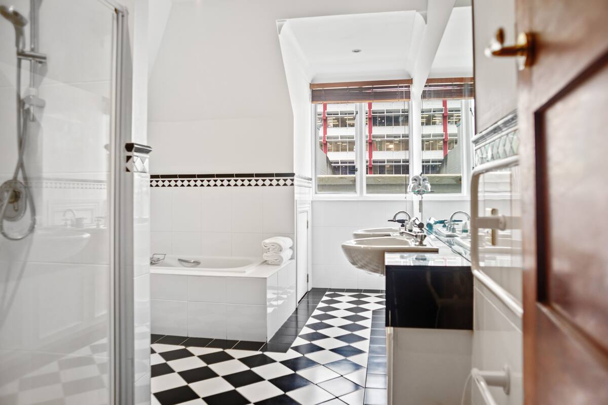 A bathroom with a checkered floor, a bathtub, a sink, and a window with a view of buildings.