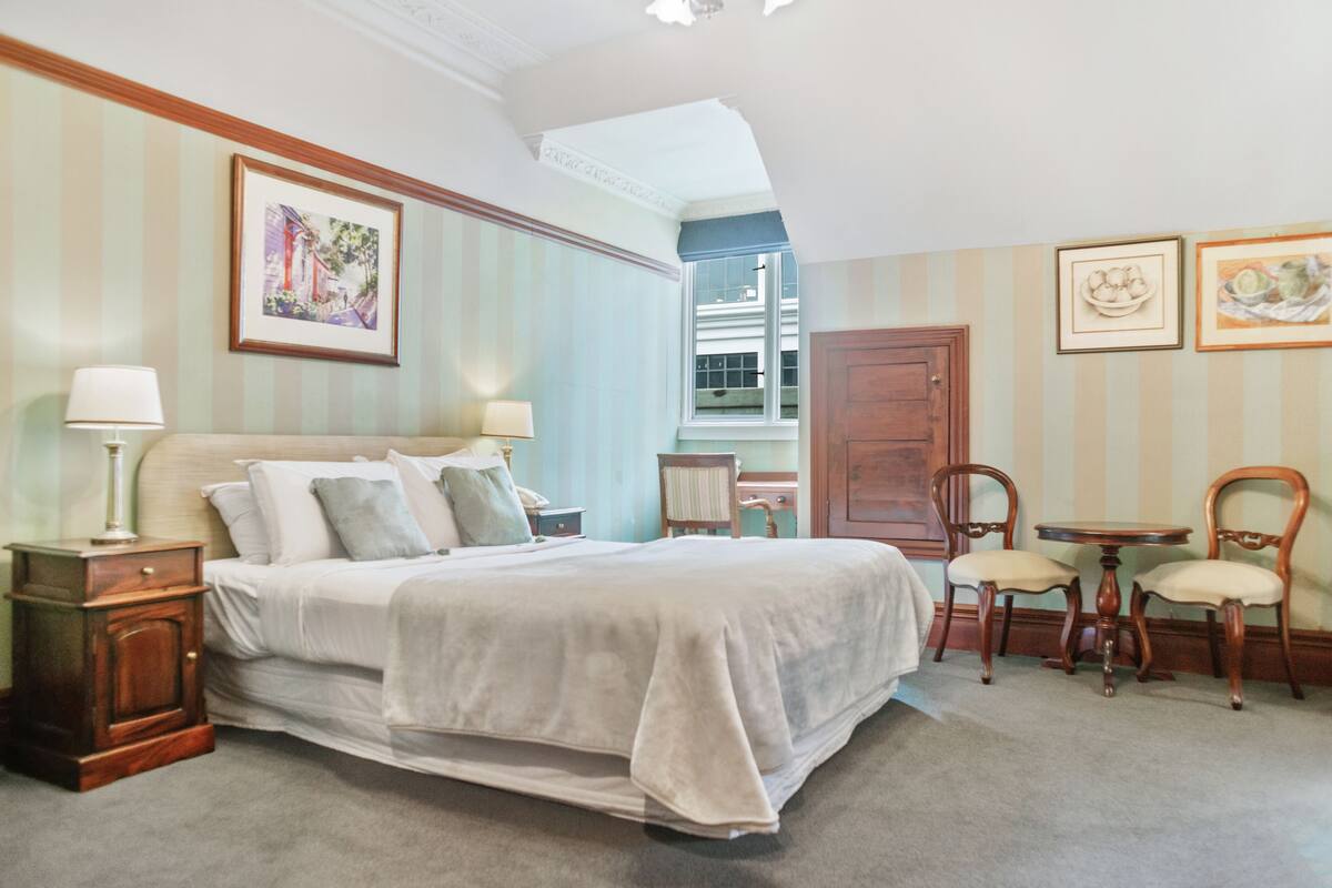 A bedroom with a large bed, two bedside tables with lamps, a window, and a door.