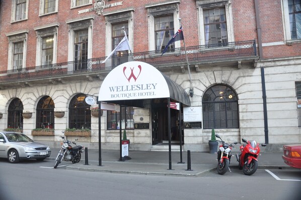 Entrada del Wellesley Boutique Hotel con un letrero, una motocicleta y un automóvil estacionados al frente.