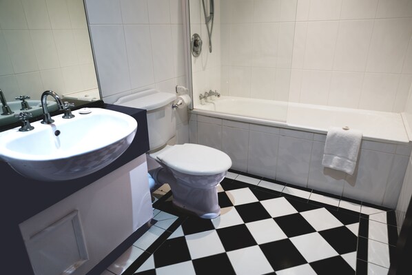 A bathroom with a white sink, toilet, and bathtub. The floor has a black and white checkered pattern.