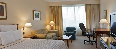 A hotel room with a large bed, a sofa, a desk with a chair, a television, and a window with curtains.