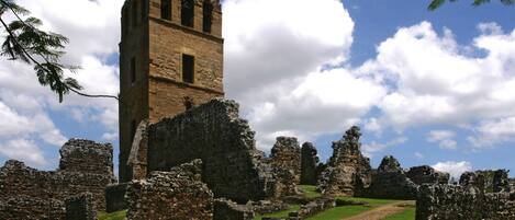 An ancient stone structure with a tower, surrounded by ruins and greenery.