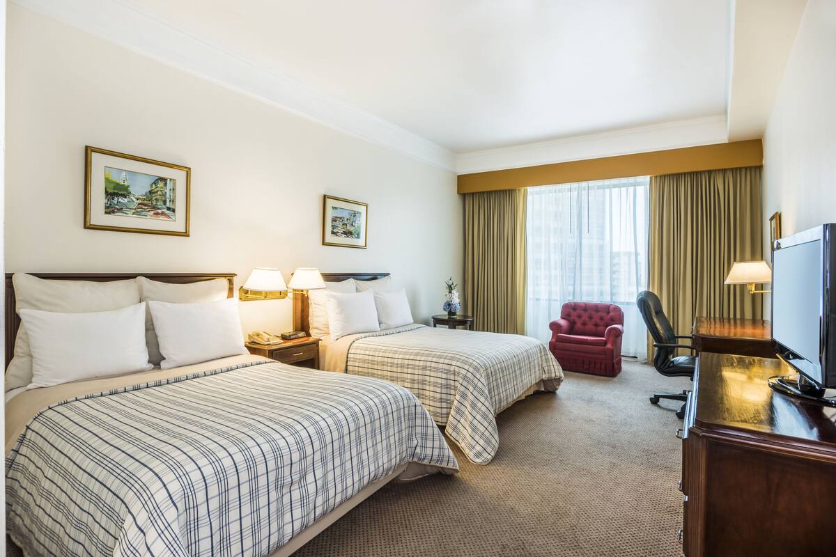 A hotel room with two beds, a desk, a TV, and a red armchair.