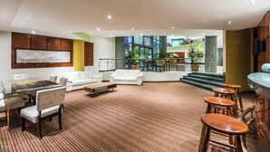 Un amplio salón con mesa de vidrio, sofás blancos y una zona de bar con taburetes.