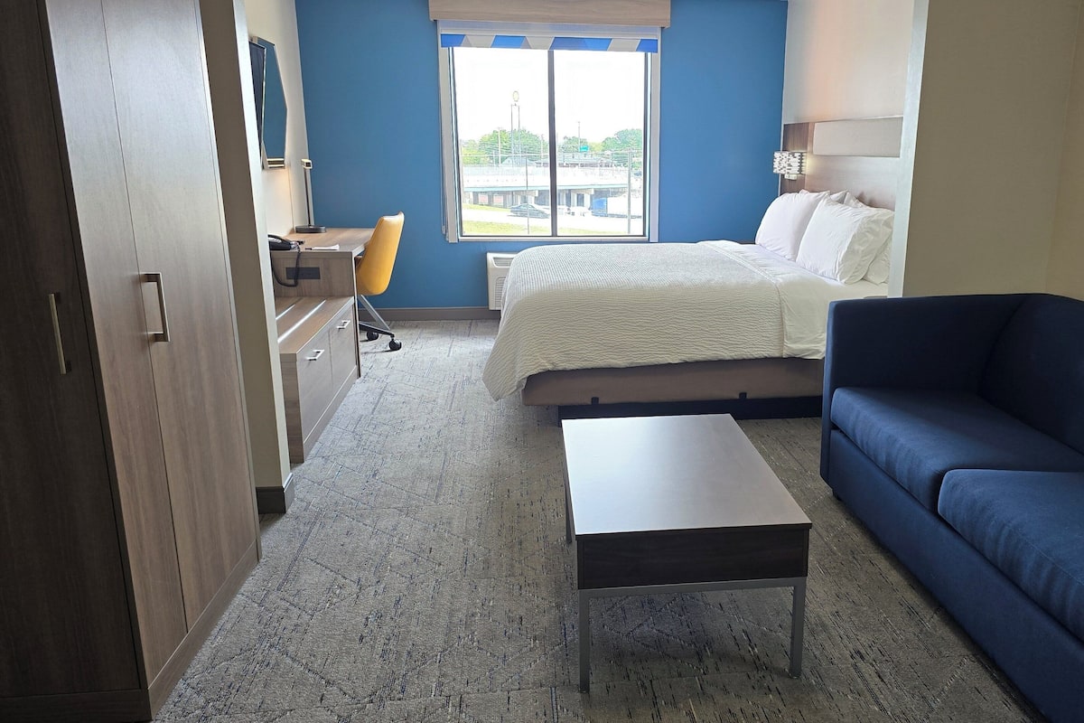 Una habitación de hotel con una cama, un sofá azul, una mesita, un escritorio con una silla y un armario.