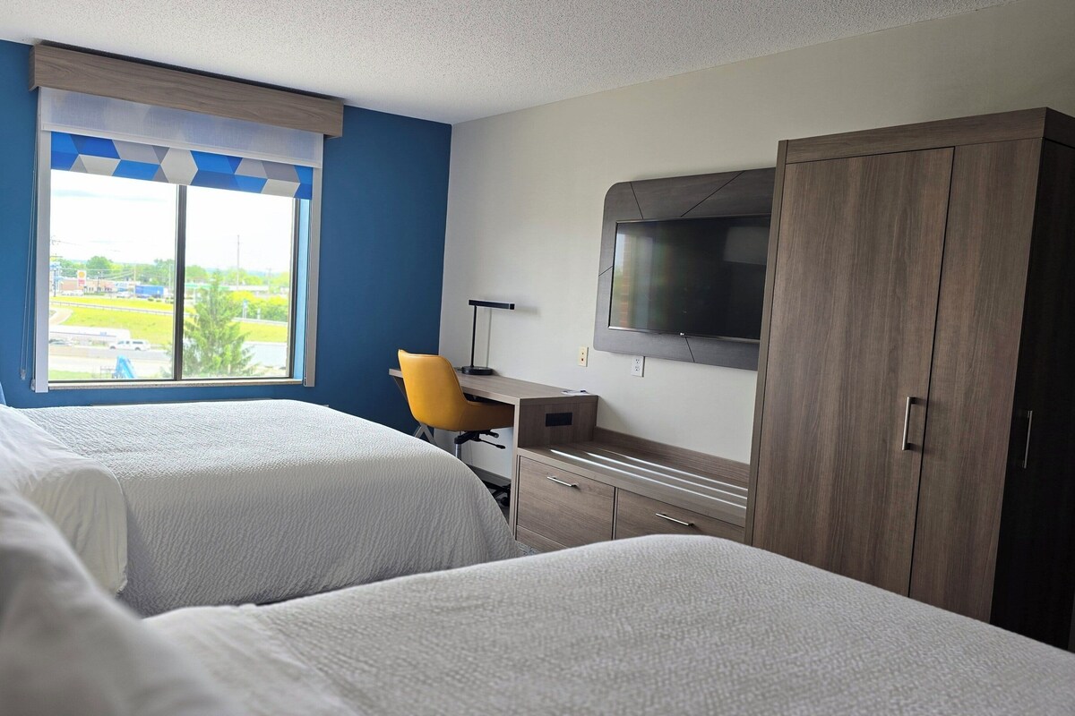 A hotel room with two beds, a desk, a chair, a TV, and a wardrobe.
