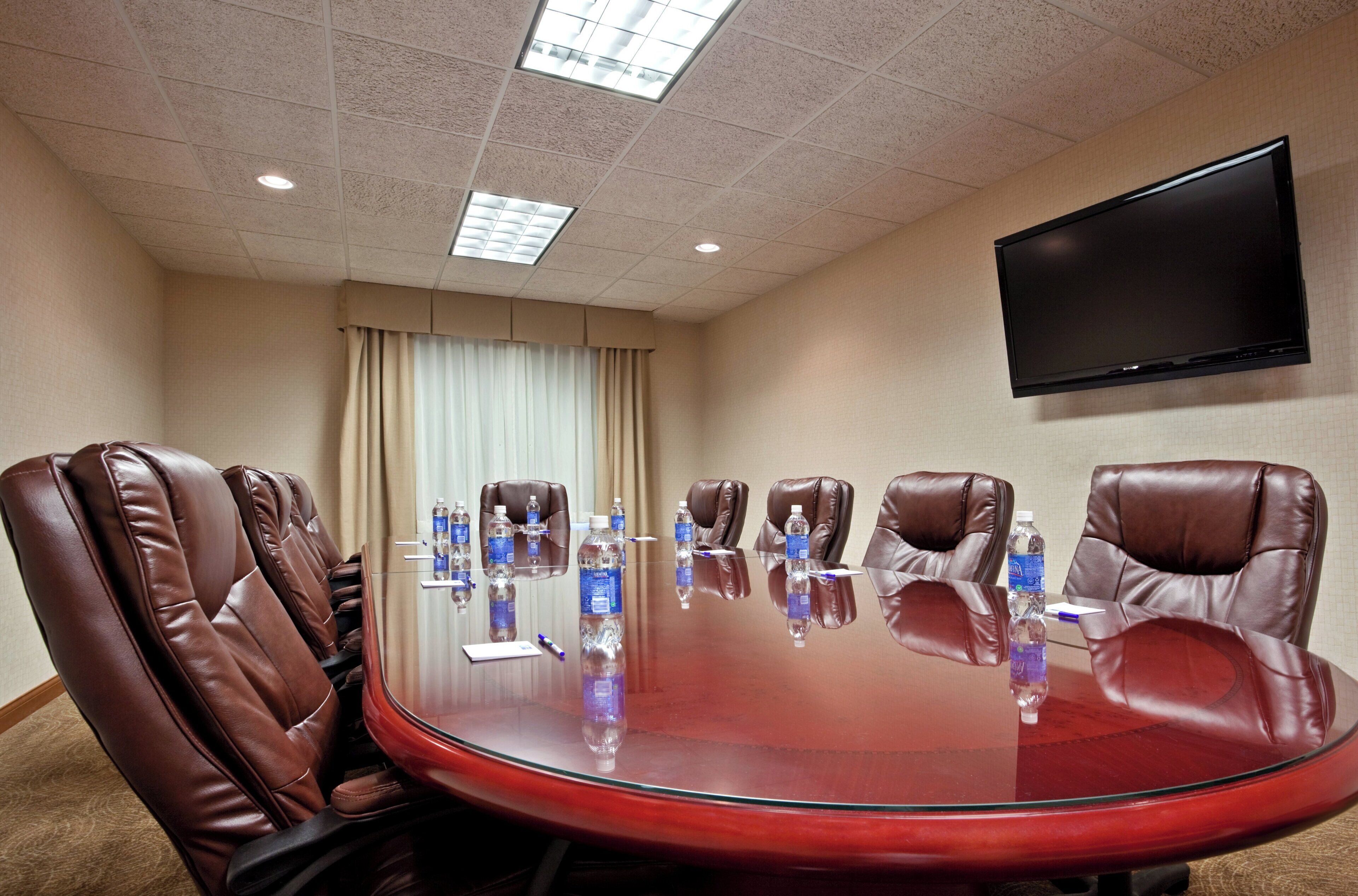 A conference room with a large oval table, leather chairs, water bottles, and a flat-screen TV on the wall.