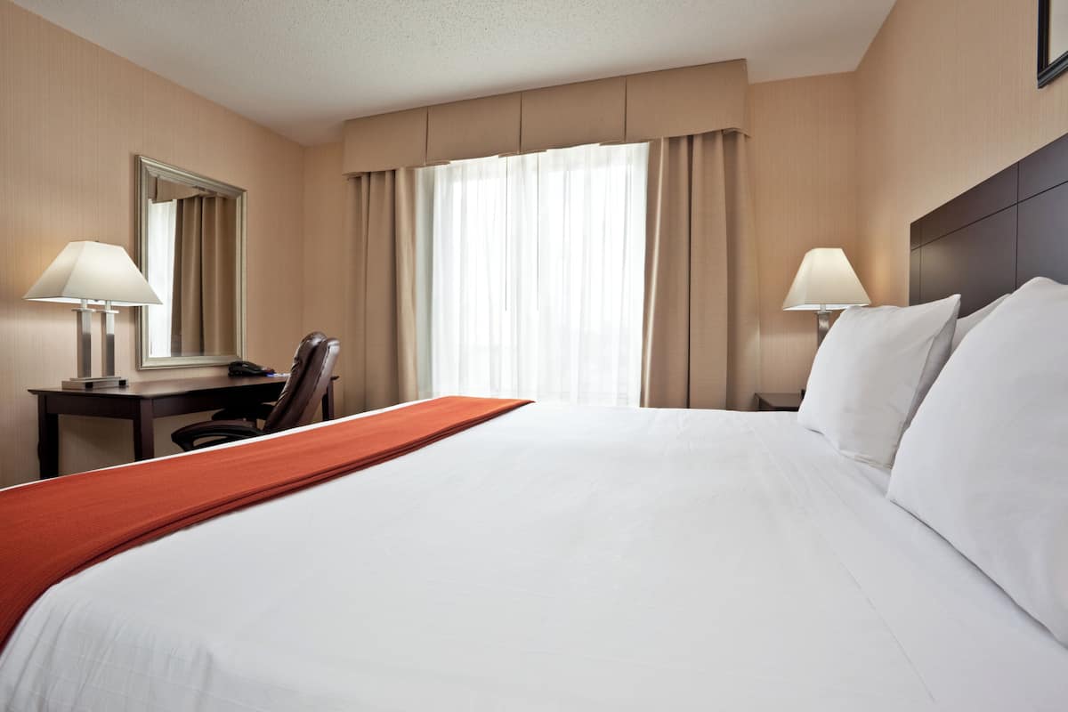 Una habitación de hotel con una cama grande, dos mesitas de noche con lámparas, un escritorio y una silla.