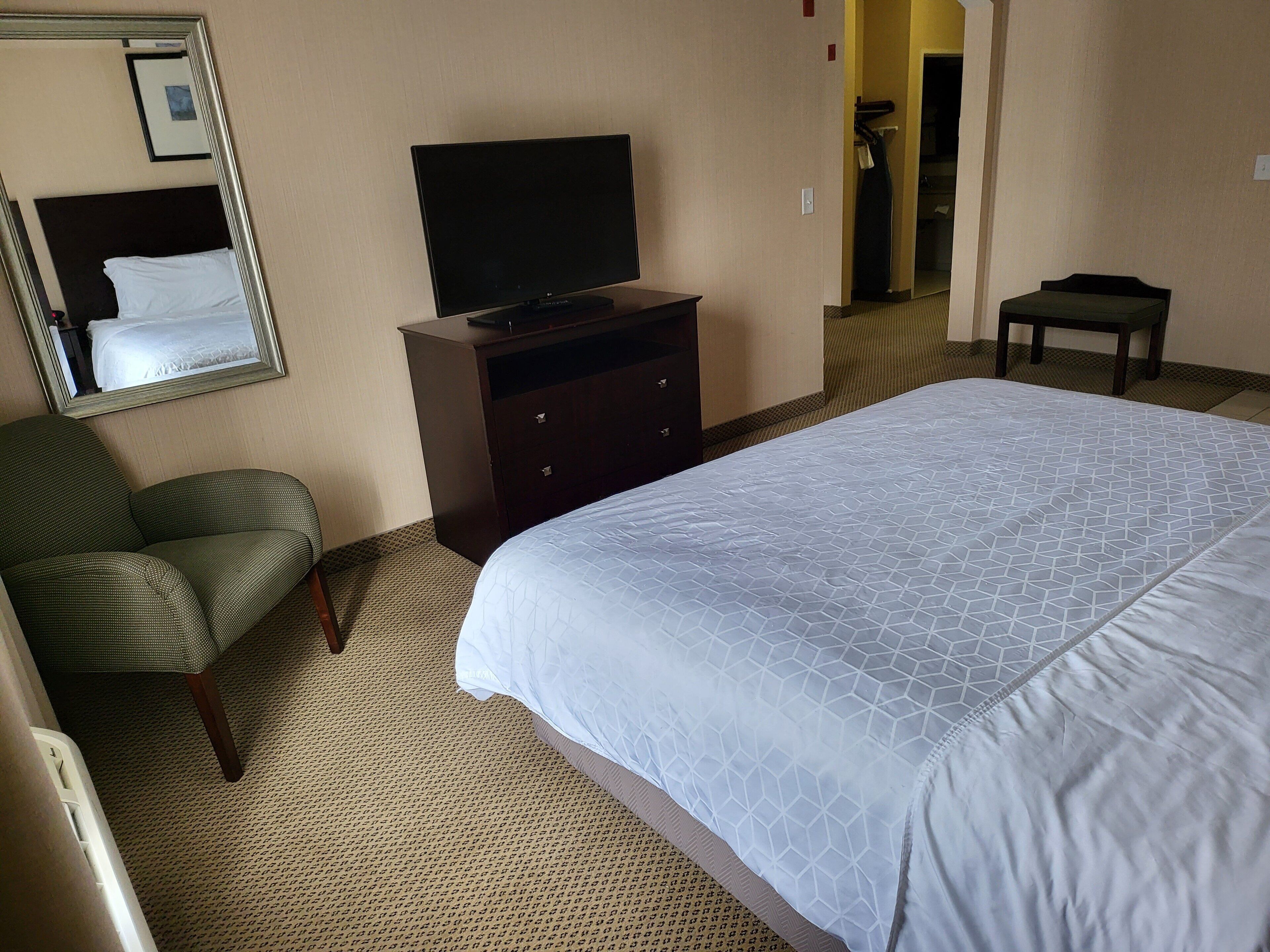 Une chambre d’hôtel avec un lit, un téléviseur posé sur une commode, une chaise et un miroir au mur.