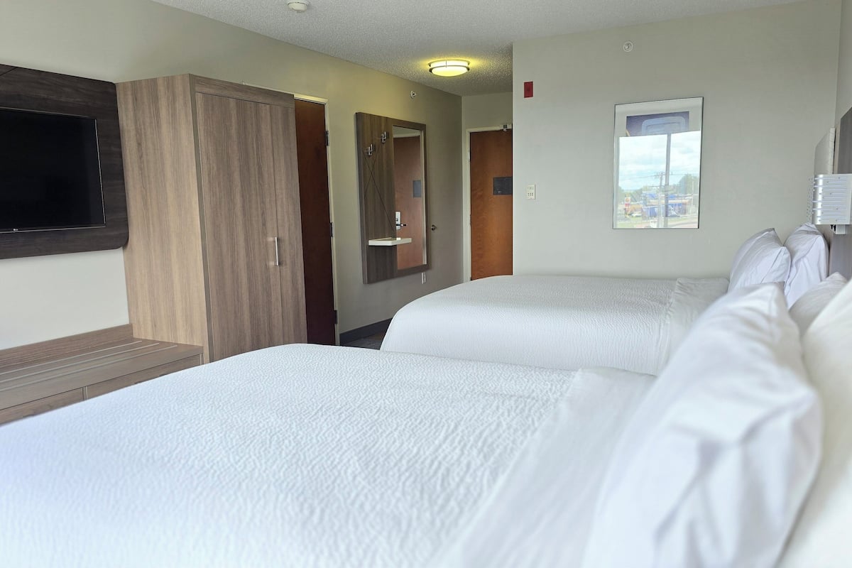 Habitación de hotel con dos camas, televisión, espejo y ventana con vista a la ciudad.