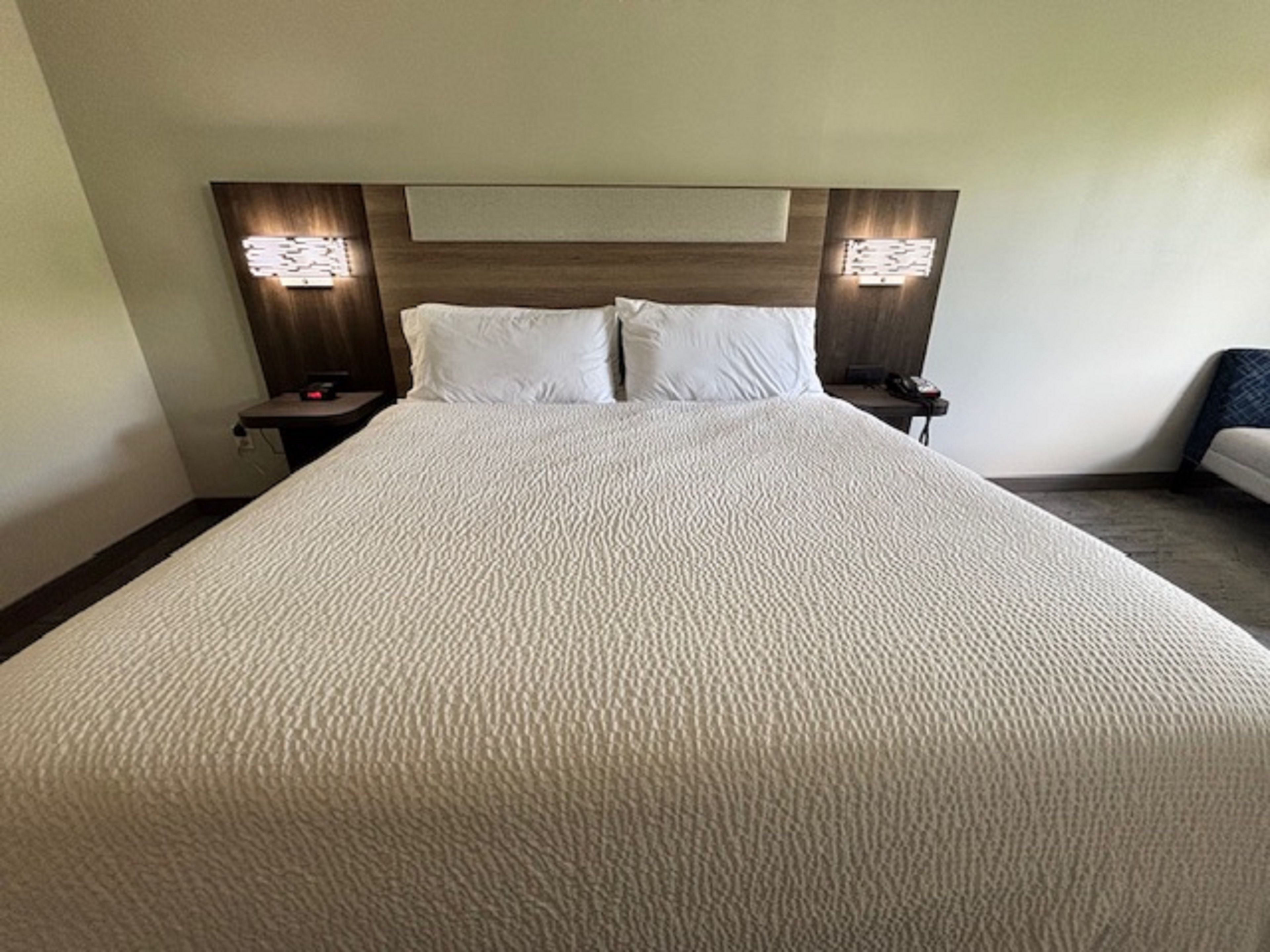 Ein großes Bett mit weißer, strukturierter Bettdecke, zwei Kissen und zwei Nachttische mit Lampen.
