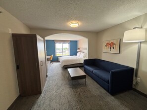 A hotel room with a bed, a desk, a chair, a sofa, and a lamp. - Holiday Inn Express Hotels and Suites Dayton North Tipp City by IHG (Tipp City)