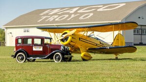 A vintage car and a yellow biplane parked in front of a building with a sign that reads "WACO TROYO". - Holiday Inn Express Hotels and Suites Dayton North Tipp City by IHG (Tipp City)