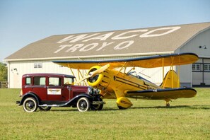 A vintage car and a yellow biplane parked in front of a building with a sign that reads "WACO TROYO". - Holiday Inn Express Hotels and Suites Dayton North Tipp City by IHG (Tipp City)