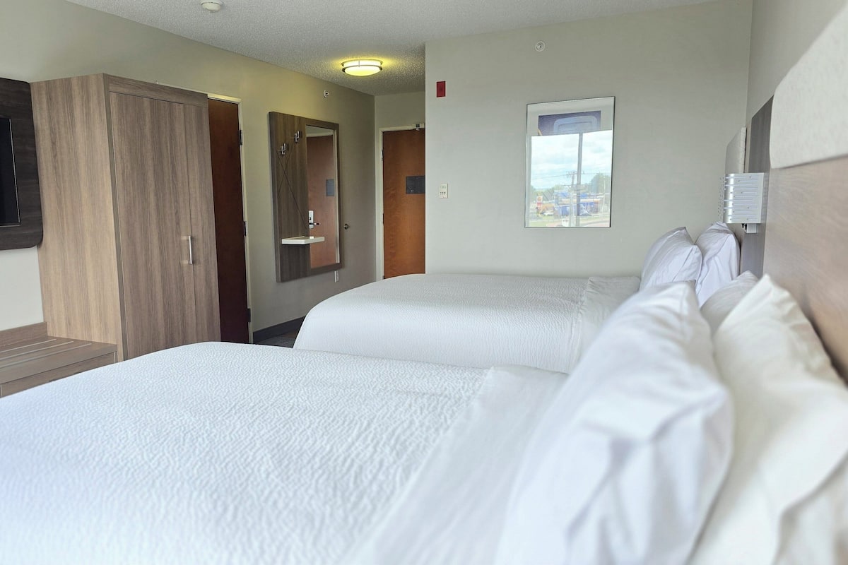 Habitación de hotel con dos camas, televisión, espejo y ventana con vistas.