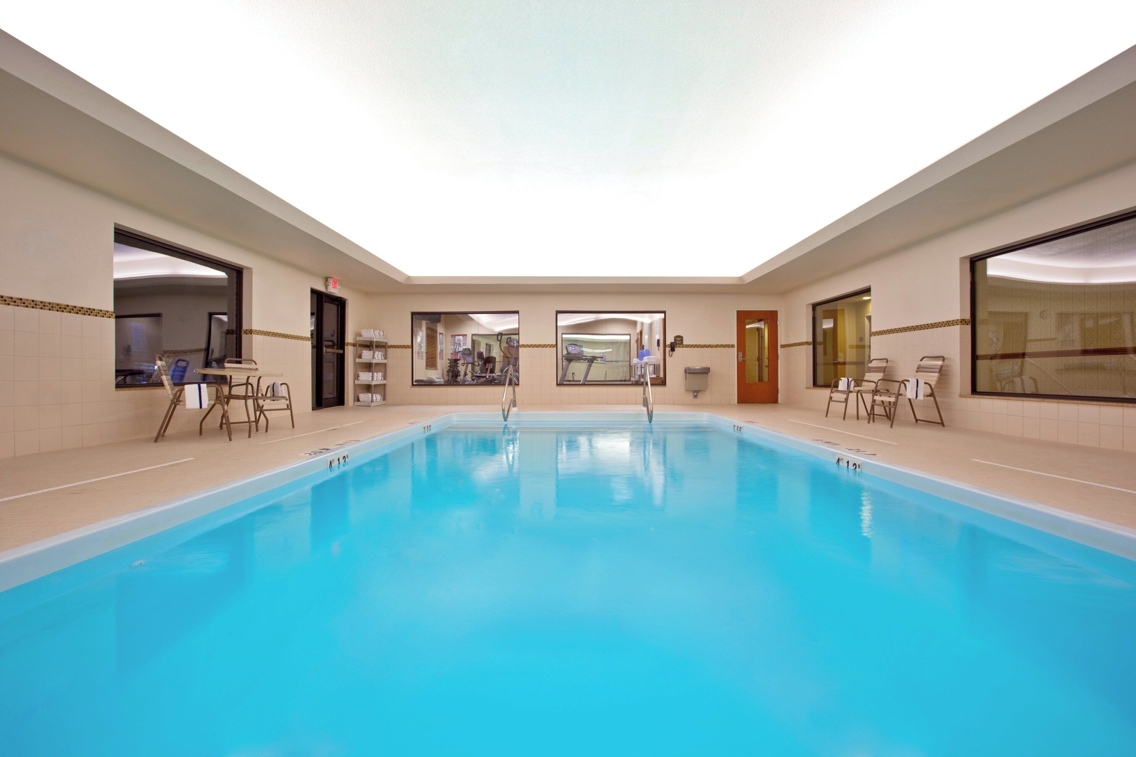 Une piscine intérieure à l’eau d’un bleu limpide, entourée de murs carrelés et équipée de matériel d’exercice.