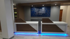 A reception desk with a modern design, featuring two counters and a blue illuminated strip at the base. - Holiday Inn Express Hotels and Suites Dayton North Tipp City by IHG (Tipp City)