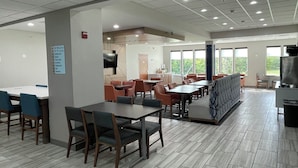 A spacious cafeteria with multiple tables and chairs, a television, and a large window providing natural light. - Holiday Inn Express Hotels and Suites Dayton North Tipp City by IHG (Tipp City)
