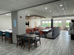 A spacious cafeteria with multiple tables and chairs, a television, and a large window providing natural light. - Holiday Inn Express Hotels and Suites Dayton North Tipp City by IHG (Tipp City)