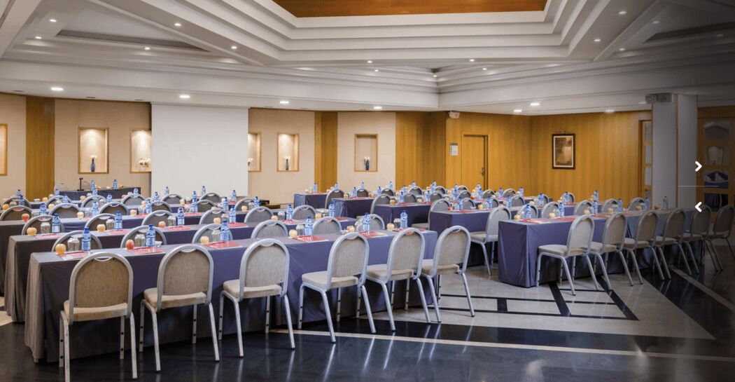 Un salón de conferencias con varias mesas y sillas, equipado con botellas de agua y tarjetas de identificación.