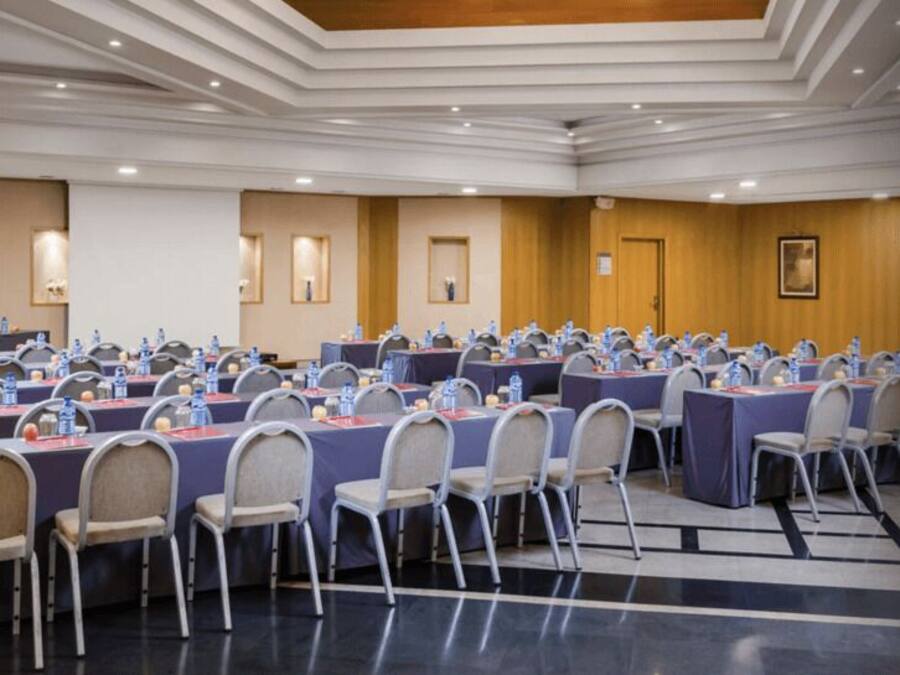 Un salón de conferencias con varias mesas y sillas, equipado con botellas de agua y tarjetas de identificación.