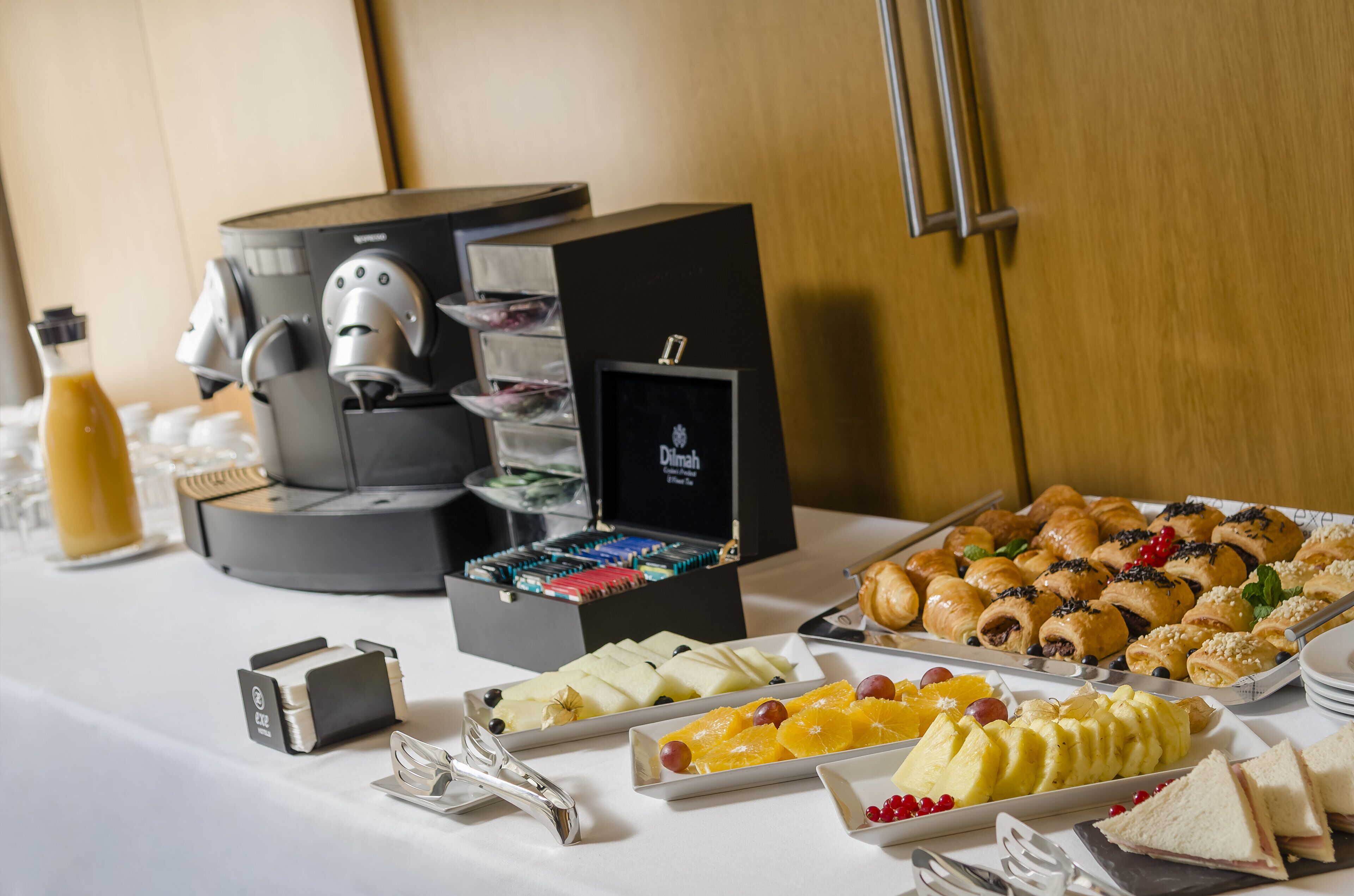 Una mesa de buffet con diversos alimentos, una máquina de café y un objeto enmarcado en la pared.