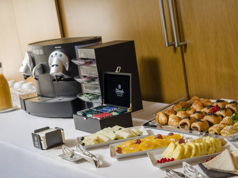 Una mesa de buffet con diversos alimentos, una máquina de café y un objeto enmarcado en la pared.