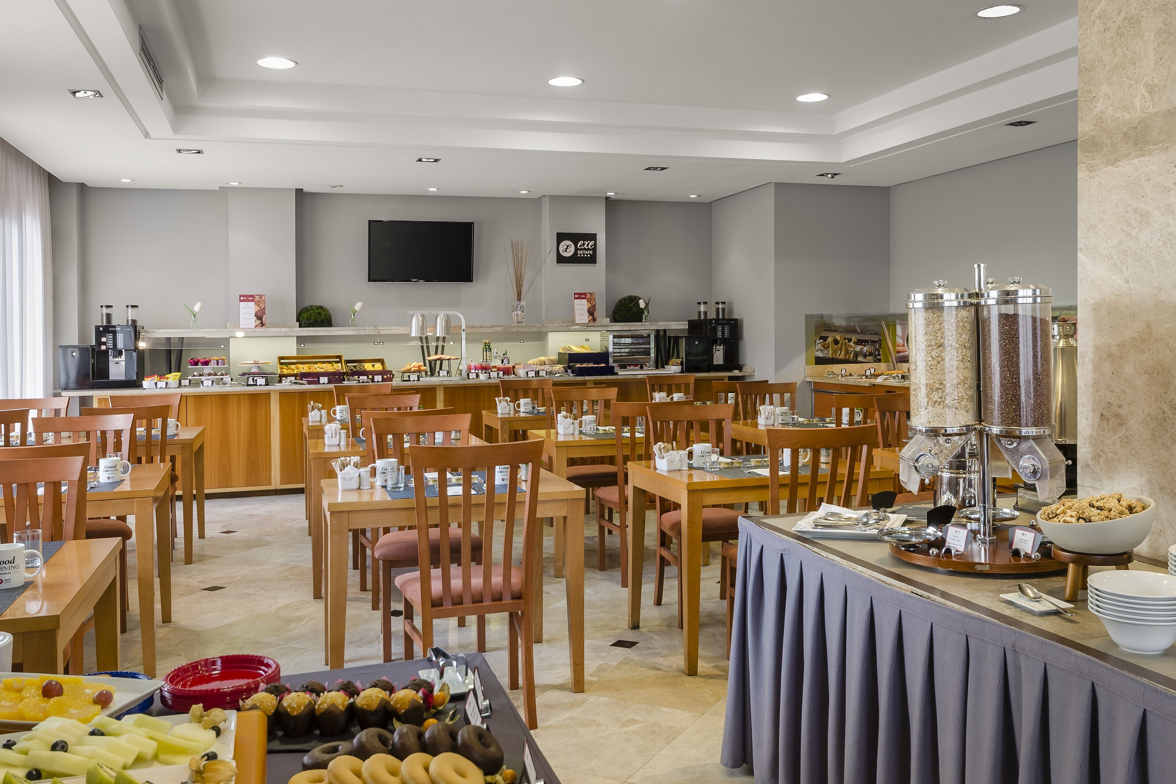 A modern breakfast area with wooden tables and chairs, a buffet counter with various food items, and a coffee station.