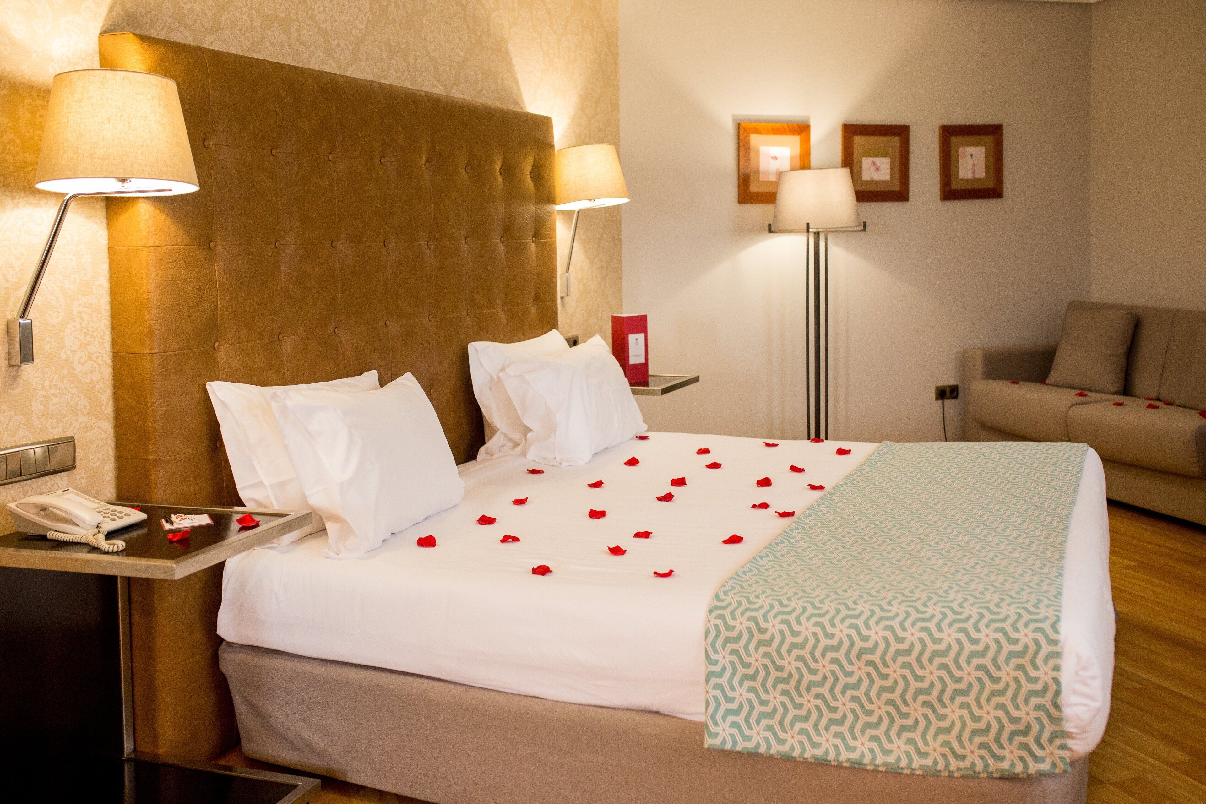 Habitación de hotel con una cama grande, dos lámparas de noche, teléfono junto a la cama y un sofá en la esquina.