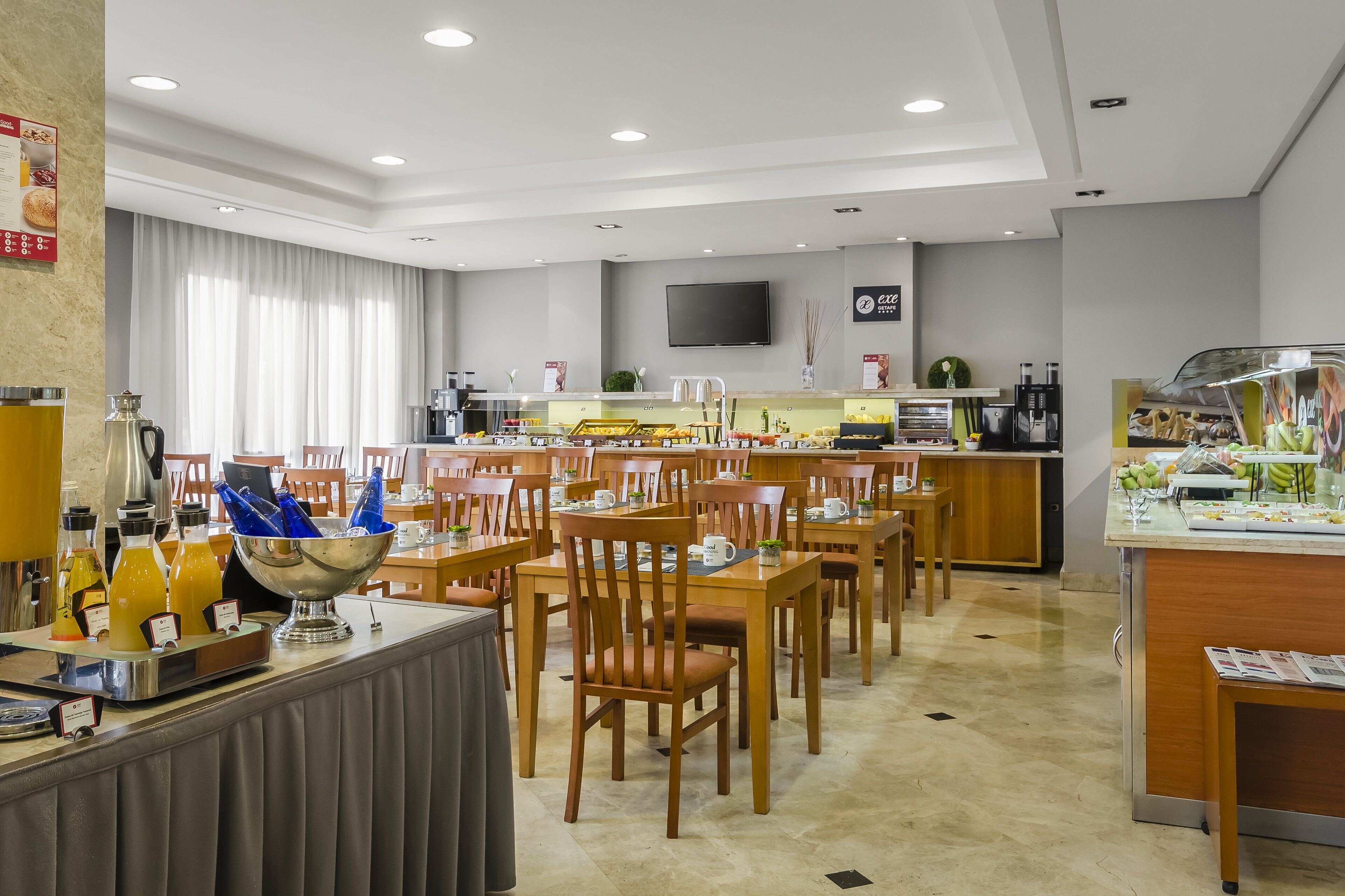Un comedor moderno de hotel con varias mesas y sillas, un mostrador de buffet y una estación de café.