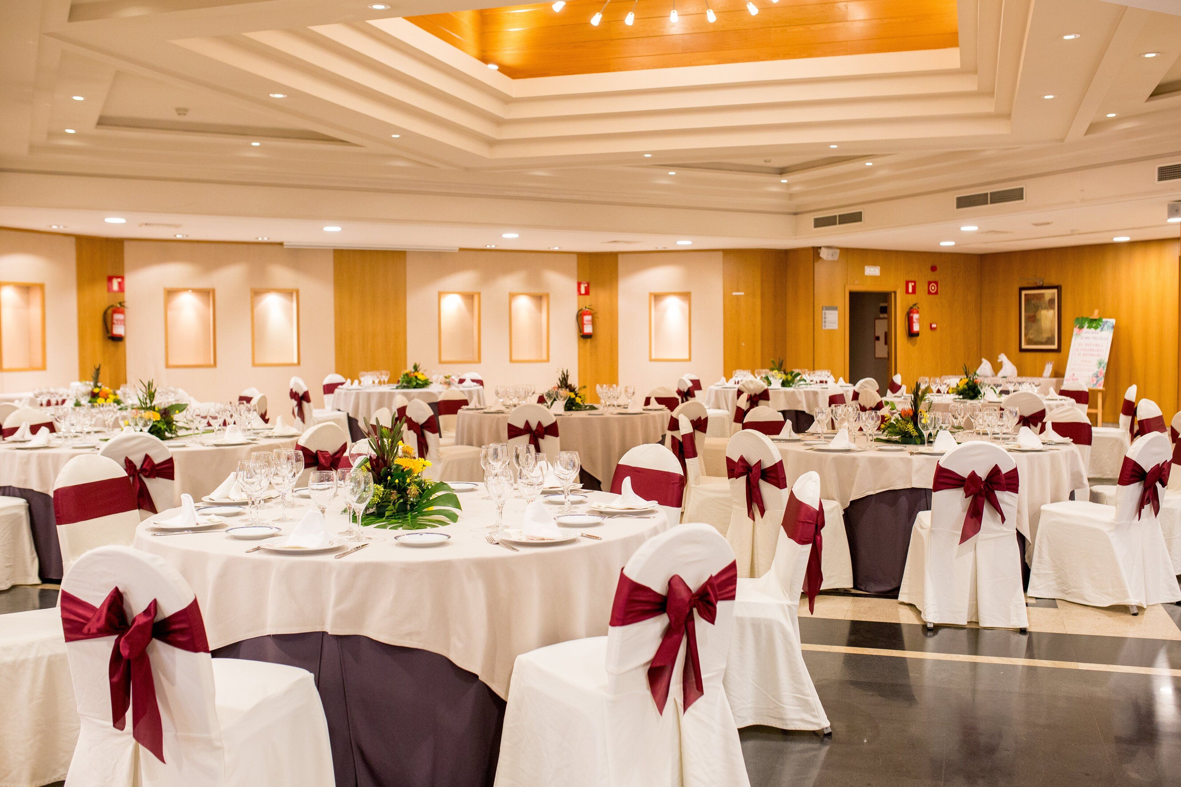 A banquet hall with round tables, white tablecloths, and chairs with red sashes.