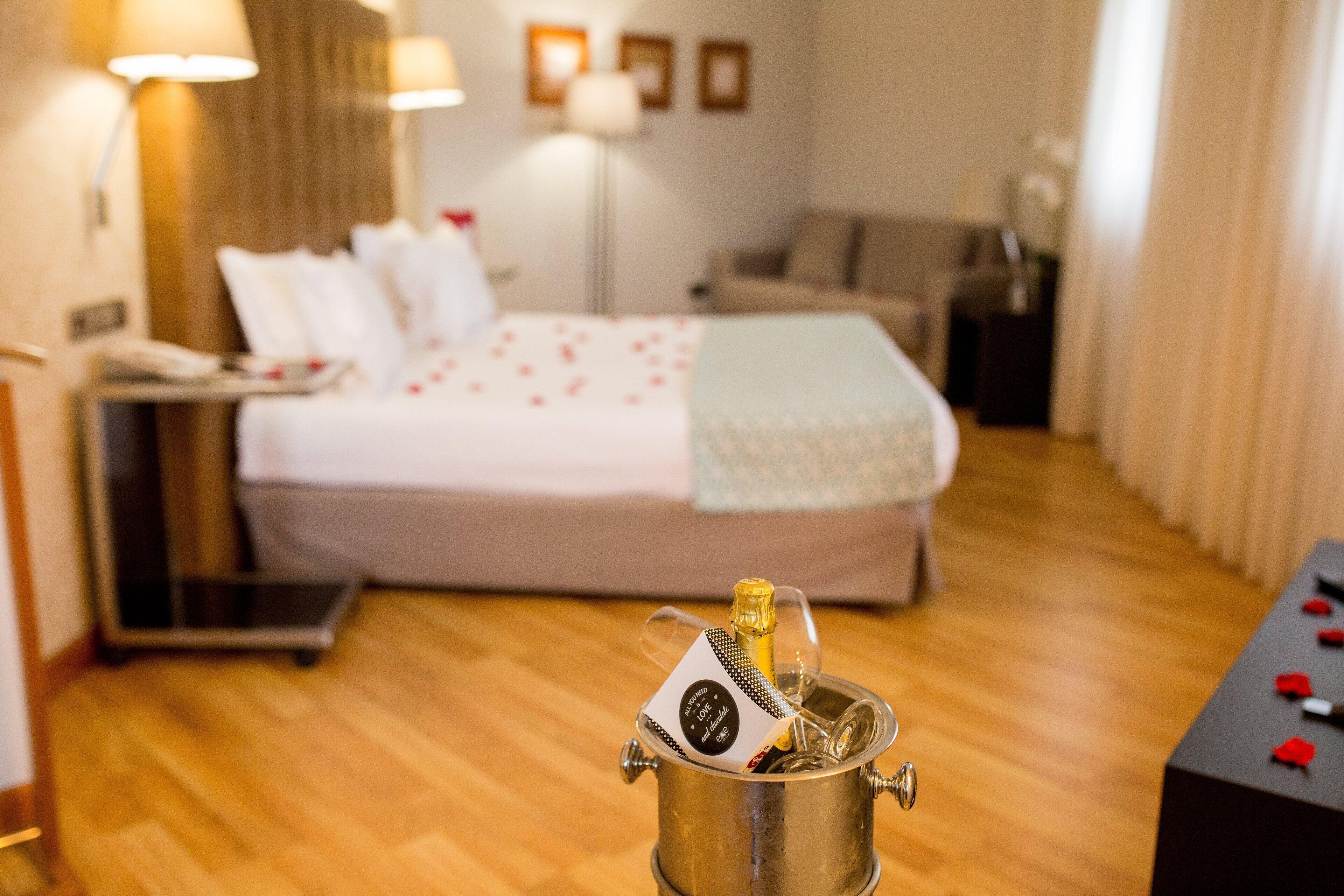 Ein Hotelzimmer mit Bett, Nachttisch, Lampe und einer Champagnerflasche in einer Kühlbox.