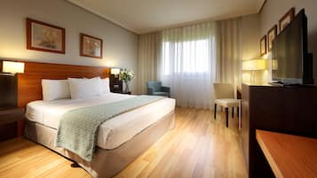 A hotel room with a large bed, a desk, a chair, a TV, and artwork on the walls.