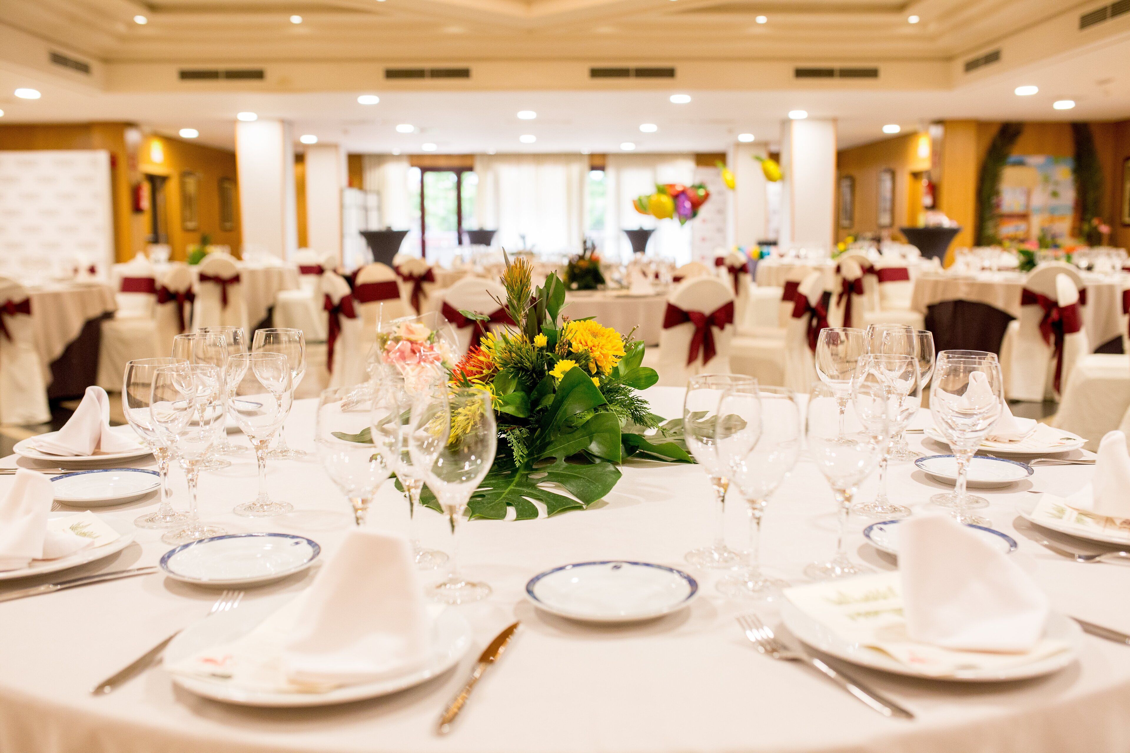 Un salón de banquetes con mesas redondas dispuestas para un evento formal, con manteles blancos, menaje impecable y centros de mesa florales.
