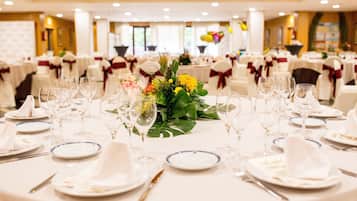 Un salón de banquetes con mesas redondas dispuestas para un evento formal, con manteles blancos, menaje impecable y centros de mesa florales.