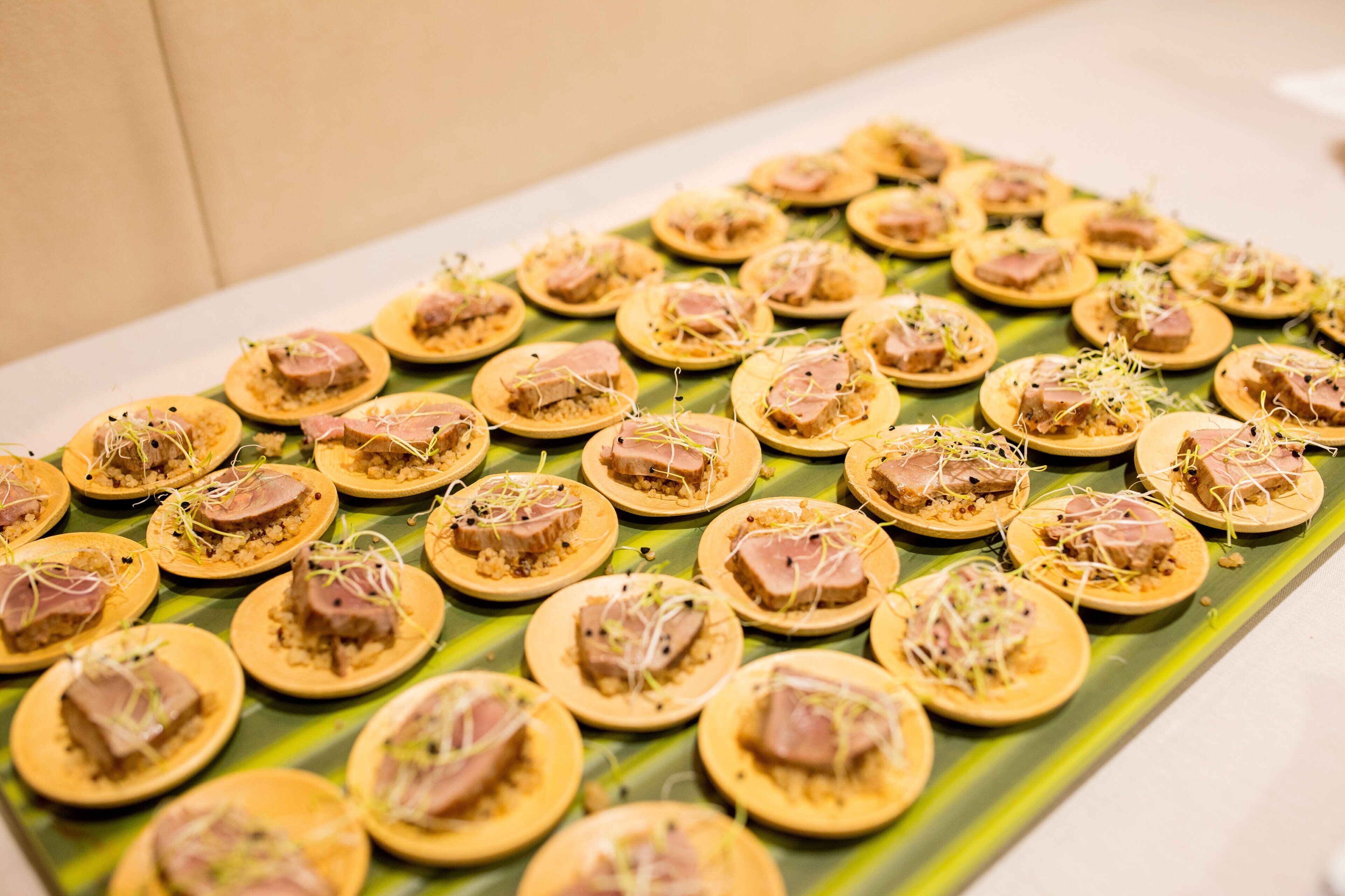 A table with round, flatbreads topped with a pinkish food item and garnished with sprouts, arranged on a green leaf-like surface.
