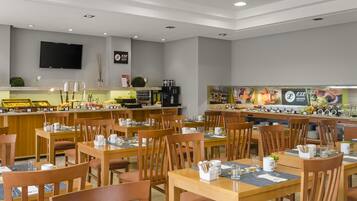 A modern restaurant with wooden tables and chairs, a buffet area, and a flat-screen TV on the wall.
