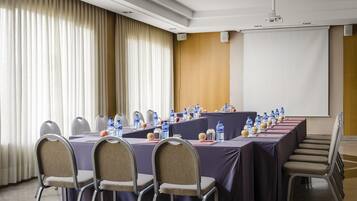 Un salón de conferencias con una larga mesa, sillas, botellas de agua y una pantalla de proyector.
