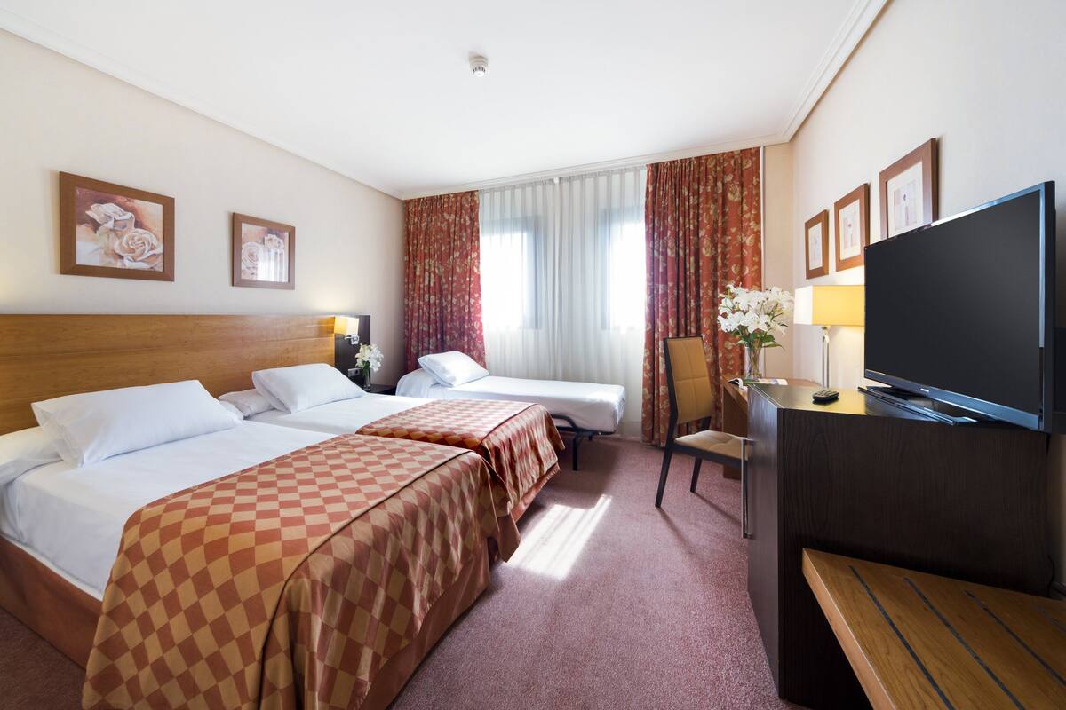 Ein Hotelzimmer mit zwei Betten, einem Schreibtisch, einem Fernseher und einem Sessel.