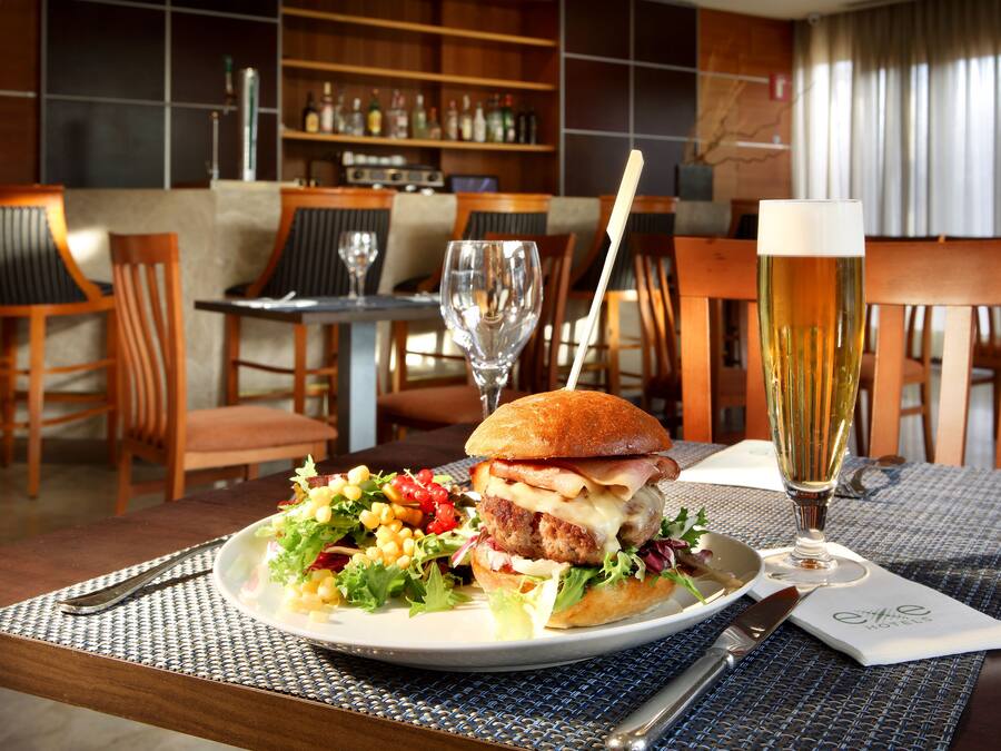 En restaurangmiljö med ett bord dukat för en måltid, inklusive en hamburgare, en sallad och ett glas öl.