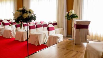 A room with rows of chairs covered in white and pink, a podium with a white tablecloth, and a red carpet.