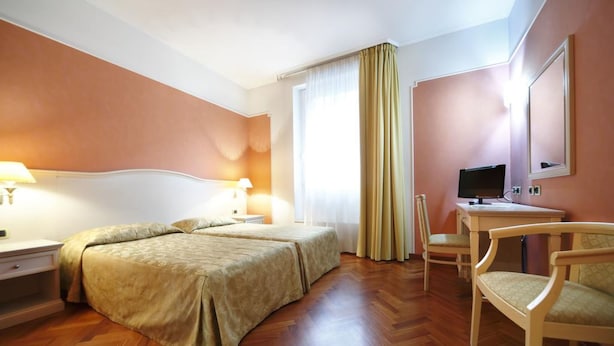 Habitación de hotel con dos camas, un escritorio, una silla, un televisor y una ventana con cortinas.