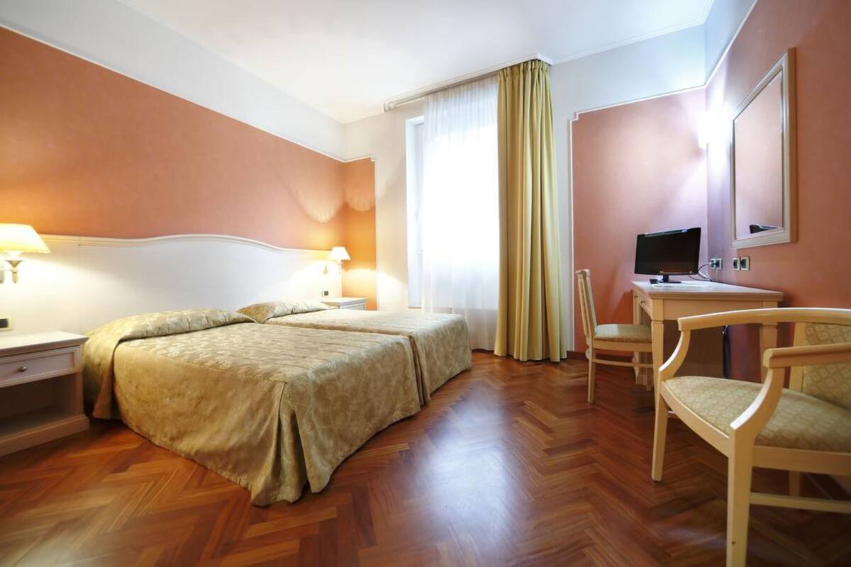 A hotel room with two beds, a desk, a chair, a television, and a window with curtains.