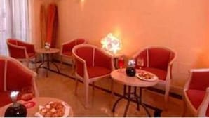 Una habitación con sillas rojas y una pequeña mesa, un televisor en la pared y una lámpara decorativa.