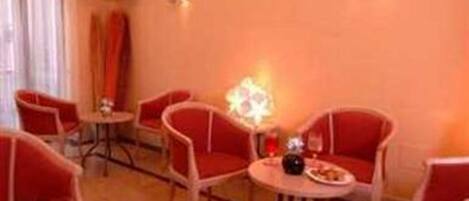 A room with red chairs and a small table, a television on the wall, and a decorative light fixture.